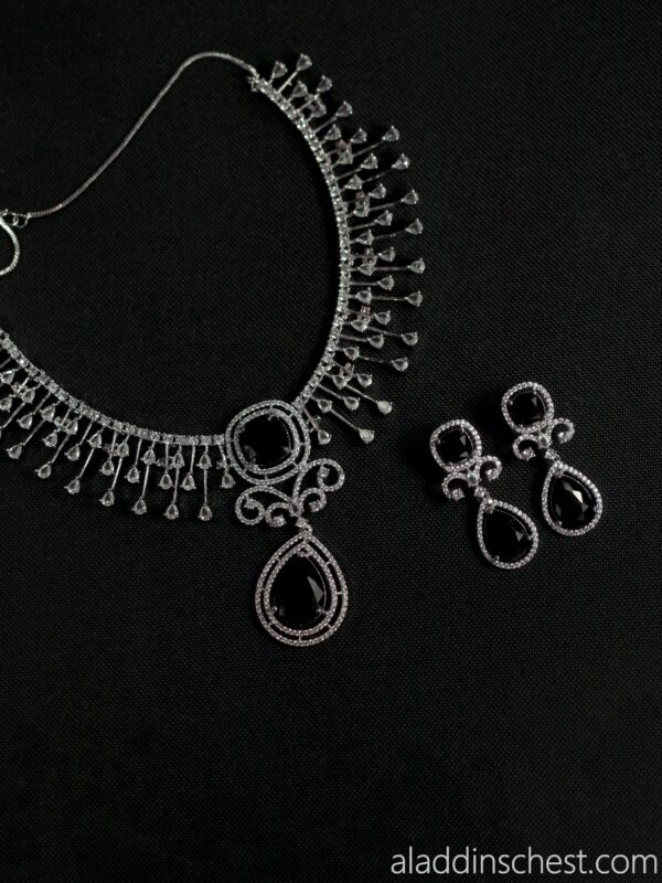 Elegant silver necklace and earrings on black background.