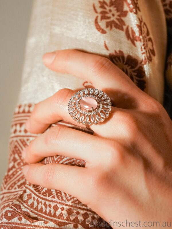 Hand wearing ornate gemstone ring on fabric background.