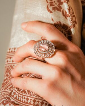 Hand wearing ornate gemstone ring on fabric background.