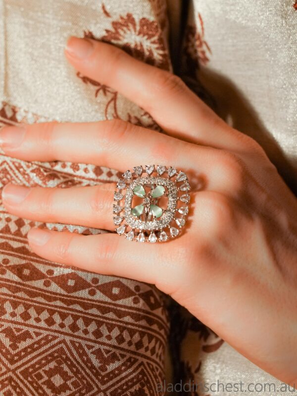 Hand wearing ornate gemstone ring on patterned fabric.