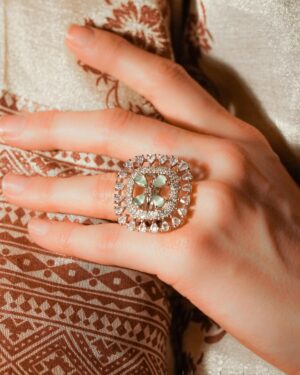 Hand wearing ornate gemstone ring on patterned fabric.