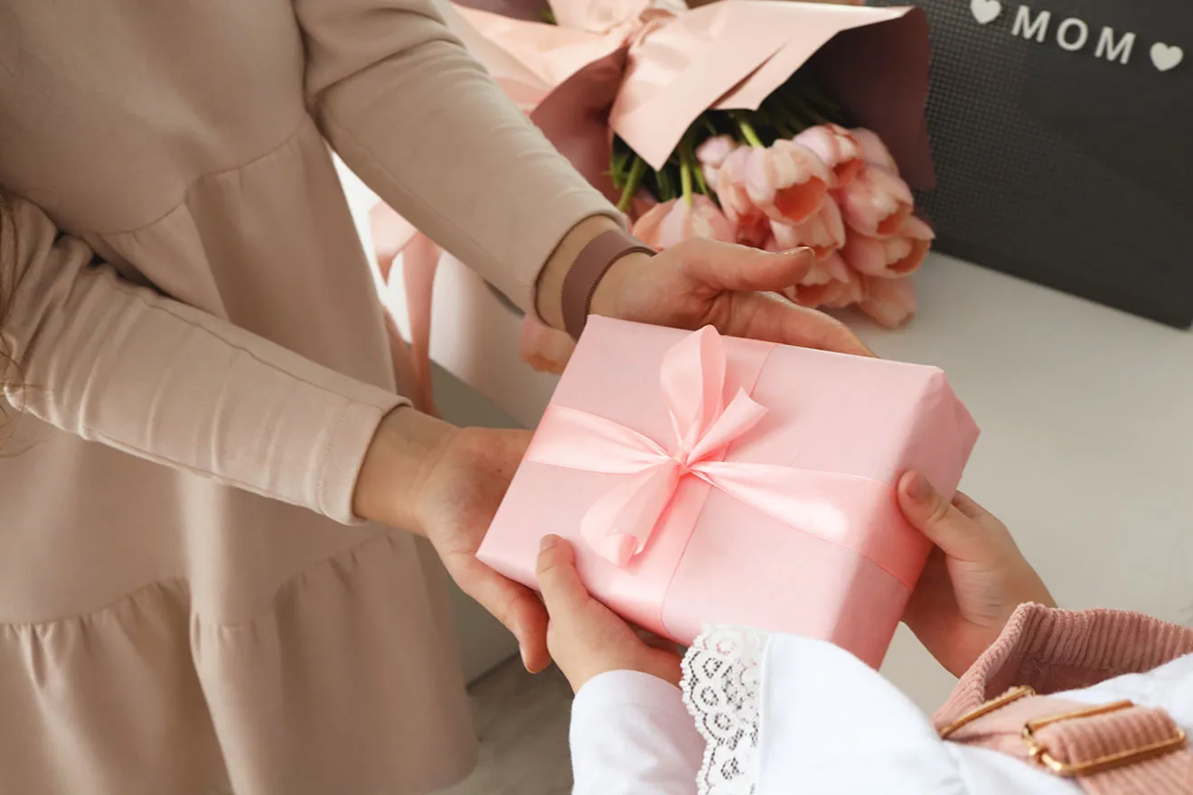 Hands exchanging pink gift box, flowers background